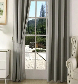 Rideaux élégants gris pour salon moderne, offrant une parfaite combinaison de style et de fonctionnalité. Ils encadrent une porte-fenêtre, laissant entrevoir un jardin verdoyant. Idéal pour ajouter une touche sophistiquée à votre décoration intérieure tout en améliorant l'intimité de votre pièce.