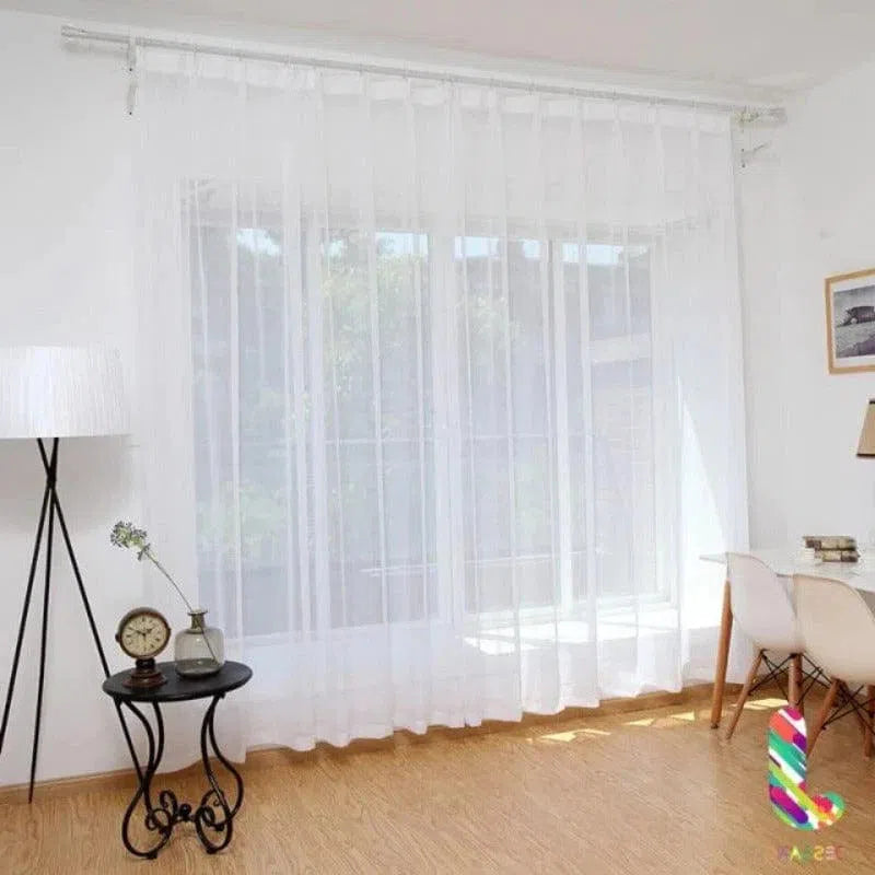 Rideau blanc translucide suspendu dans un salon lumineux avec sol en bois, flanqué d'une table d'appoint noire et d'une chaise moderne, apportant une touche élégante et épurée à la décoration intérieure.