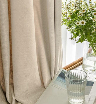 Rideaux élégants dans un intérieur lumineux, accompagnés d'un vase de fleurs blanches et d'un verre d'eau sur une table, créant une atmosphère apaisante et accueillante. Idéal pour ajouter une touche de raffinement et de fraîcheur à votre décoration d'intérieur.