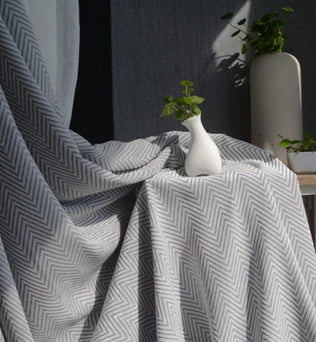 Rideau élégant à motifs chevrons gris et blanc, drapé devant une fenêtre, avec une décoration contemporaine. Idéal pour ajouter une touche de sophistication et de style moderne à n'importe quelle pièce. Composition en tissu de haute qualité, offrant un effet d'ombrage efficace. Accessoire de décoration intérieure, parfait pour salon, chambre ou bureau.