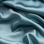 Tissu bleu élégant avec reflets lumineux, offrant une texture soyeuse et ondulée, idéal pour la confection de vêtements de luxe ou de linge de maison raffiné.