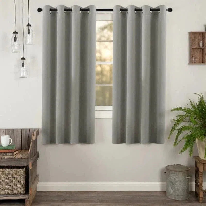 Rideau occultant gris élégant avec œillets, idéal pour une décoration moderne de salon. Ce rideau de haute qualité offre une solution efficace pour bloquer la lumière et assurer l'intimité. Parfait pour un intérieur contemporain, il est présenté dans une pièce joliment décorée, complétée par des luminaires suspendus et des plantes d'intérieur. Convient pour embellir différentes pièces, de la chambre au bureau.