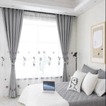 Chambre moderne avec rideaux élégants et couvre-lit gris, ornée de coussins décoratifs et éclairée par une lampe de lecture. Ambiance lumineuse grâce à une grande fenêtre habillée de voilages blancs. Parfaite pour créer un espace reposant et sophistiqué, idéal pour travailler ou se détendre. Design intérieur contemporain mettant en valeur le confort et l'esthétique.