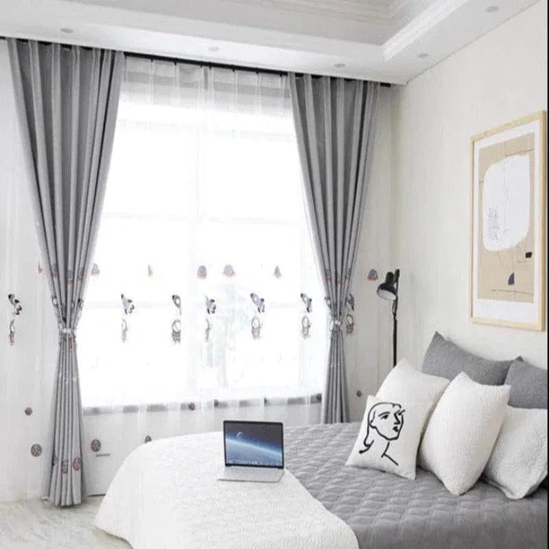 Chambre moderne avec rideaux élégants et couvre-lit gris, ornée de coussins décoratifs et éclairée par une lampe de lecture. Ambiance lumineuse grâce à une grande fenêtre habillée de voilages blancs. Parfaite pour créer un espace reposant et sophistiqué, idéal pour travailler ou se détendre. Design intérieur contemporain mettant en valeur le confort et l'esthétique.