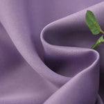 Gros plan sur un tissu violet avec une texture douce, accompagné d'une touche de vert apportée par une feuille, idéal pour la mode et la décoration d'intérieur élégante et moderne.