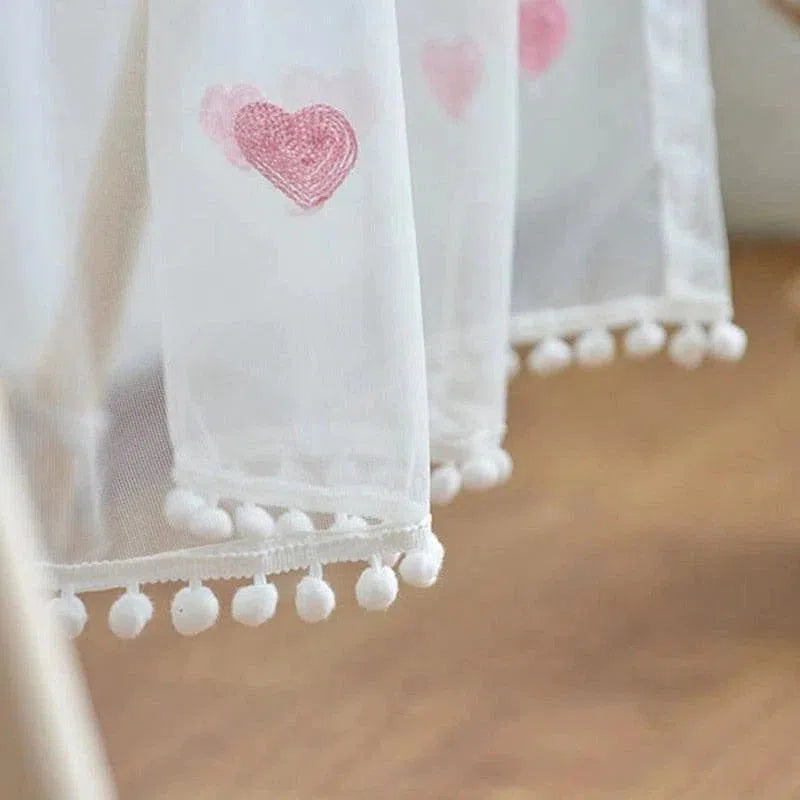 Rideau décoratif blanc avec motifs de cœurs roses et bordures à pompons, idéal pour apporter une touche romantique et délicate à votre intérieur. Ce rideau élégant s'intègre parfaitement dans une chambre d'enfant ou un salon, ajoutant une ambiance douce et accueillante. Parfait pour ceux qui recherchent à combiner style et convivialité dans leur décoration.