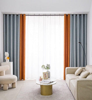 Salon moderne avec canapé beige et table basse design, décoré de rideaux gris et orange. Ambiance lumineuse grâce à une grande fenêtre, complétée par un fauteuil contemporain et un lampadaire élégant. Parfait pour un intérieur chic et accueillant.
