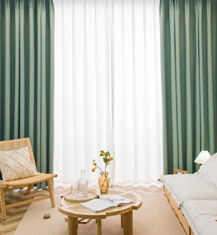 Salon moderne avec décor minimaliste. Rideaux verts et blancs en arrière-plan, meubles en bois clair, fauteuil et canapé confortables. Table basse avec vase et livres, ambiance lumineuse et apaisante idéale pour la détente et la lecture.