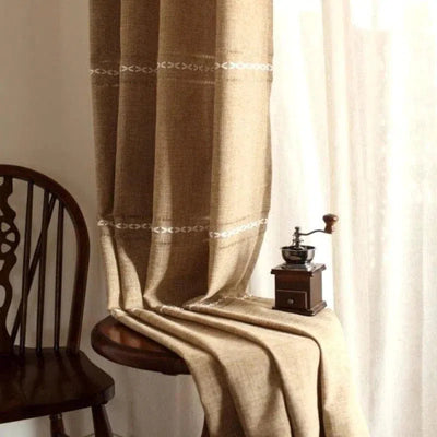 Rideau élégant de couleur beige avec motifs brodés subtils, idéal pour ajouter une touche chaleureuse et accueillante à votre intérieur. Accessoire de décoration parfait pour le salon, la chambre ou la salle à manger, offrant une ambiance cosy. Accessoire complémentaire à côté d'une chaise en bois classique et d'un moulin à café vintage.