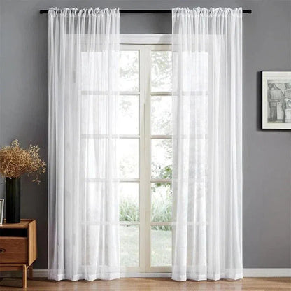 Rideau blanc transparent suspendu à une tringle noire devant une fenêtre à battants, créant une ambiance lumineuse et épurée dans un salon moderne avec un mur gris, un meuble en bois et une décoration minimaliste.