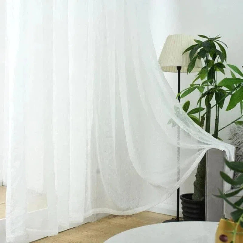 Rideau blanc élégant pour salon moderne, filtrant la lumière naturelle. Décoration intérieure avec plante verte et lampe sur pied. Ambiance chaleureuse et apaisante pour maison contemporaine.
