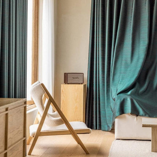 Chaise design minimaliste avec structure en bois, placée dans un salon moderne. Rideaux élégants de couleur verte encadrant une grande fenêtre offrant une vue lumineuse. Ambiance épurée et chaleureuse, idéale pour optimiser la décoration intérieure d'un espace de détente.