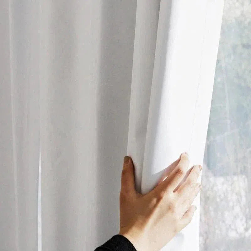 Main tenant un rideau blanc devant une fenêtre, illustrant une décoration intérieure lumineuse et épurée. Rideau moderne idéal pour ajouter une touche élégante à votre salon ou chambre.