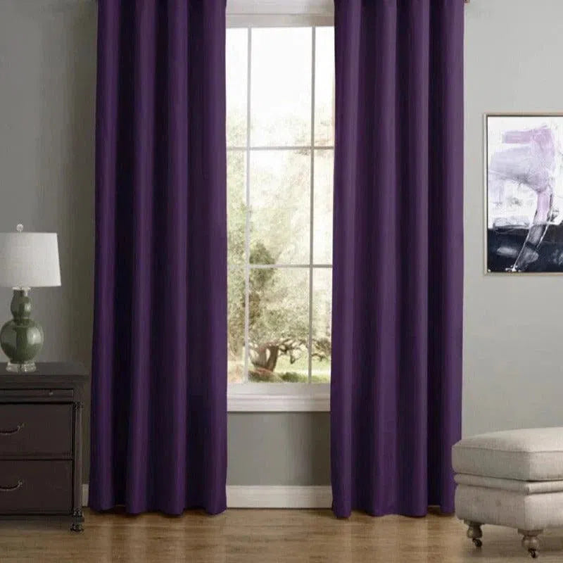 Rideaux violets en décoration d'intérieur élégante, cadeaux devant une grande fenêtre dans un salon moderne avec murs gris, mettant en valeur une lampe sur une table de chevet et un fauteuil confortable, créant une atmosphère chaleureuse et sophistiquée.