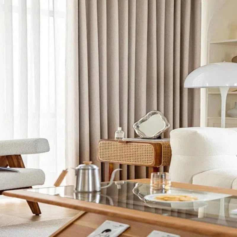 Salon moderne avec rideaux élégants et mobilier scandinave. Un fauteuil confortable et une lampe design complètent ce décor chaleureux. La table basse en verre ajoute une touche sophistiquée, entourée d'un intérieur lumineux et épuré. Idéal pour un style contemporain et accueillant.