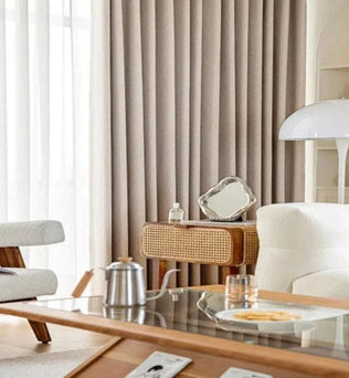 Salon moderne avec rideaux élégants et mobilier scandinave. Un fauteuil confortable et une lampe design complètent ce décor chaleureux. La table basse en verre ajoute une touche sophistiquée, entourée d'un intérieur lumineux et épuré. Idéal pour un style contemporain et accueillant.