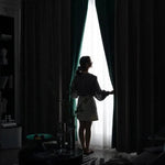 Femme ouvrant des rideaux sombres dans un salon élégant, permettant à la lumière naturelle d'entrer. Ambiance harmonieuse grâce à la décoration intérieure moderne. Atmosphère accueillante et chic, idéale pour profiter de moments de détente à la maison.