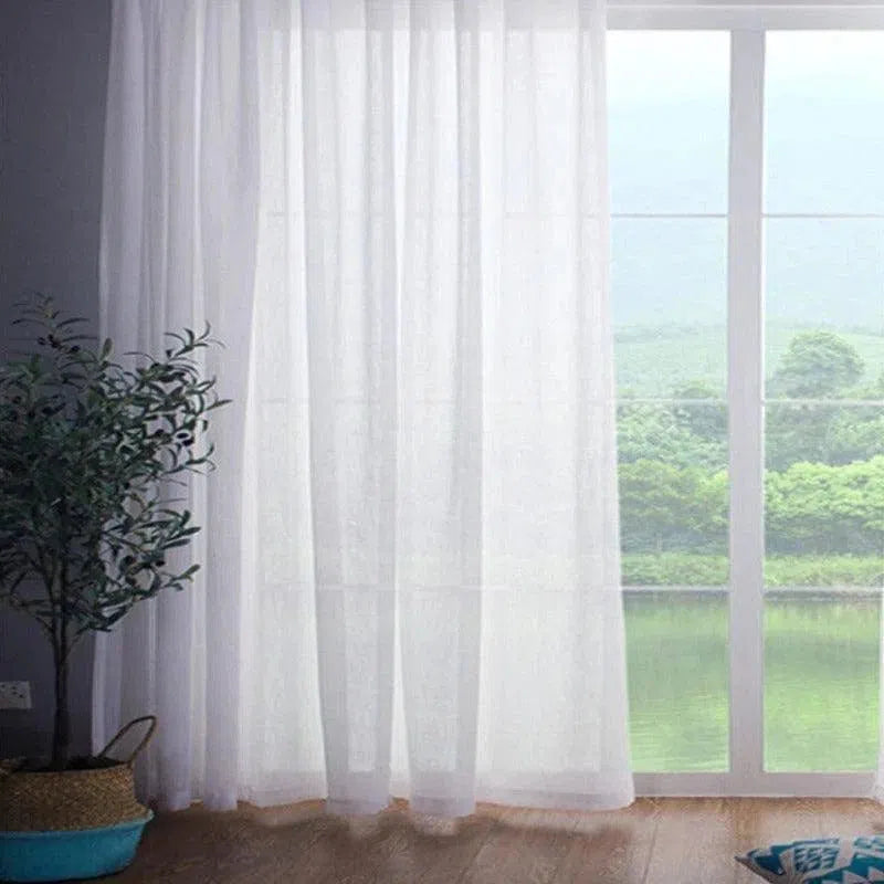 Rideau blanc translucide devant une grande baie vitrée laissant entrer la lumière naturelle. Vue sur un paysage verdoyant, avec un sol en bois et une plante d'intérieur en pot à gauche. Ambiance apaisante et lumineuse pour un intérieur moderne et élégant. Idéal pour ajouter une touche de légèreté et de fraîcheur à votre décoration.