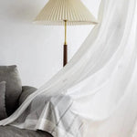 Rideau blanc élégant avec motifs délicats, installé près d'un canapé gris et d'une lampe à pied, apportant une touche moderne et lumineuse à la décoration intérieure.