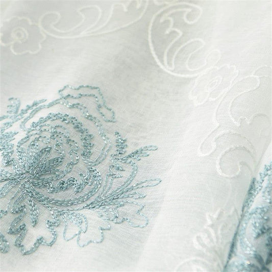 Détail d'une broderie élégante sur tissu, mettant en valeur un motif floral bleu subtil et raffiné, idéal pour la décoration intérieure et le design textile. Cette conception ajoute une touche de sophistication et de charme classique à tout espace de vie.