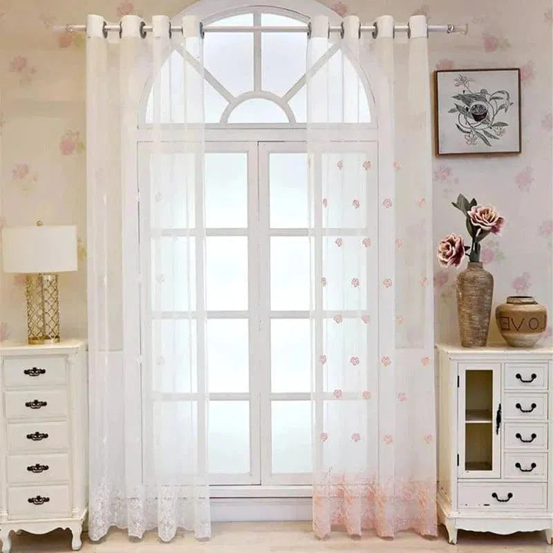 Rideaux élégants et transparents avec motif floral rose, parfaits pour éclairer et embellir une pièce. Idéal pour une décoration intérieure raffinée, cet habillage de fenêtre complète un mobilier classique avec deux commodes blanches, des fleurs décoratives et un tableau mural, créant une ambiance harmonieuse et accueillante.