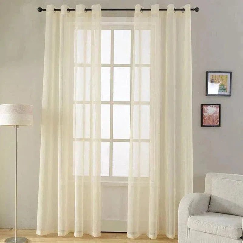 Rideau transparent pour salon moderne, couleur ivoire, accroché à une tringle noire, idéal pour laisser passer la lumière. Intégré dans une décoration intérieure épurée, soulignant une fenêtre à double battant, avec un canapé gris clair et une lampe sur pied élégante. Parfait pour créer une ambiance lumineuse et accueillante dans votre maison.