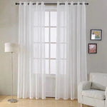 Rideaux blancs élégants pour salon moderne, ajoutant luminosité et élégance à votre intérieur. Ils sont suspendus à une tringle noire devant une grande fenêtre. Décoration épurée avec un canapé confortable, une lampe sur pied et des tableaux muraux. Idéal pour créer une ambiance chaleureuse et accueillante.