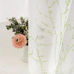 Rideau décoratif avec motif végétal vert, parfait pour une ambiance naturelle et élégante dans votre intérieur. Idéal pour apporter une touche de fraîcheur et de modernité à vos espaces. Accessoire d'intérieur stylé avec fleurs en arrière-plan.