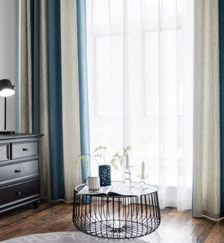 Rideaux élégants pour salon, style moderne et chic, couleurs harmonieuses bleu et beige, lumière naturelle filtrée, ambiance sereine, table basse circulaire en métal noir avec décorations, mobilier contemporain et éclairage subtile.