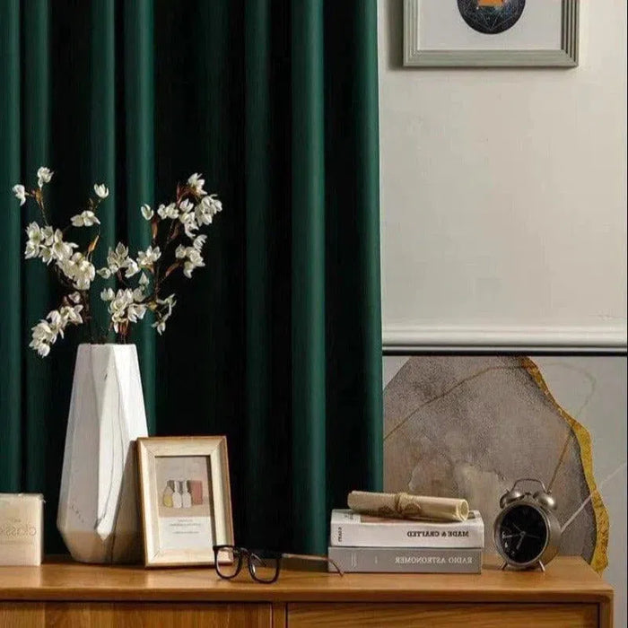 Rideau occultant vert foncé élégant, idéal pour salon ou chambre. Décoration moderne avec vase blanc et fleurs, réveil vintage et livres sur buffet en bois. Ambiance cosy et sophistiquée.