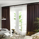 Rideaux élégants en tissu marron foncé habillant de grandes fenêtres dans un salon moderne. Décoration intérieure chic avec une luminosité naturelle filtrée par les rideaux doubles combinant opacité et voile pour gérer la lumière ambiante. Idéal pour un design contemporain et chaleureux.