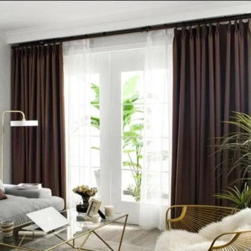 Rideaux élégants en tissu marron foncé habillant de grandes fenêtres dans un salon moderne. Décoration intérieure chic avec une luminosité naturelle filtrée par les rideaux doubles combinant opacité et voile pour gérer la lumière ambiante. Idéal pour un design contemporain et chaleureux.