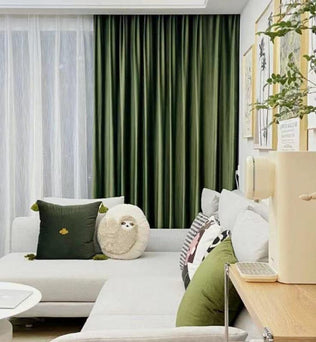 Salon moderne avec rideaux verts, canapé gris clair avec coussins décoratifs. Décoration murale tendance avec cadres, ambiance accueillante et confortable idéale pour se détendre.