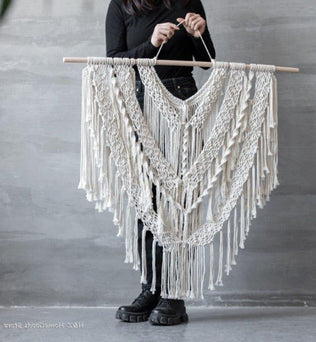 Décoration murale en macramé de style bohème suspendue à une tige en bois. Élément décoratif idéal pour apporter une touche artistique et élégante à votre intérieur. Conçu avec des motifs complexes et des franges, ce macramé s’adapte parfaitement à un salon moderne ou une chambre cosy.