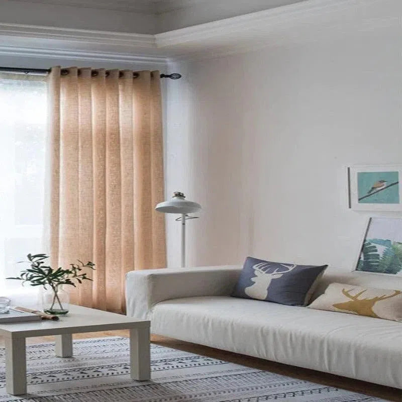 Salon moderne et lumineux avec rideaux beige, canapé confortable, coussins décoratifs à motifs animaliers et lampe élégante, créant une ambiance cosy et accueillante.