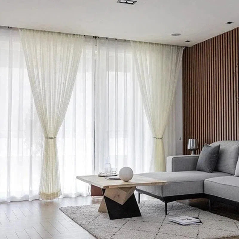 Salon moderne avec rideaux blancs élégants et canapé d'angle. Cet espace de vie spacieux est agrémenté d'un tapis doux et d'une table basse contemporaine, offrant une ambiance lumineuse et accueillante. Idéal pour les aménagements intérieurs raffinés et confortables.