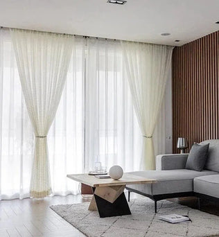 Salon moderne avec rideaux blancs élégants et canapé d'angle. Cet espace de vie spacieux est agrémenté d'un tapis doux et d'une table basse contemporaine, offrant une ambiance lumineuse et accueillante. Idéal pour les aménagements intérieurs raffinés et confortables.