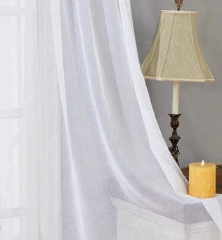 Voilage blanc élégant pour fenêtre, offrant une atmosphère lumineuse et apaisante à votre intérieur. Idéal pour illuminer le salon ou la chambre tout en préservant l'intimité. Accessoire décoratif parfait pour compléter un décor classique avec une touche de chaleur grâce aux éléments de la pièce, comme la lampe vintage et la bougie décorative.