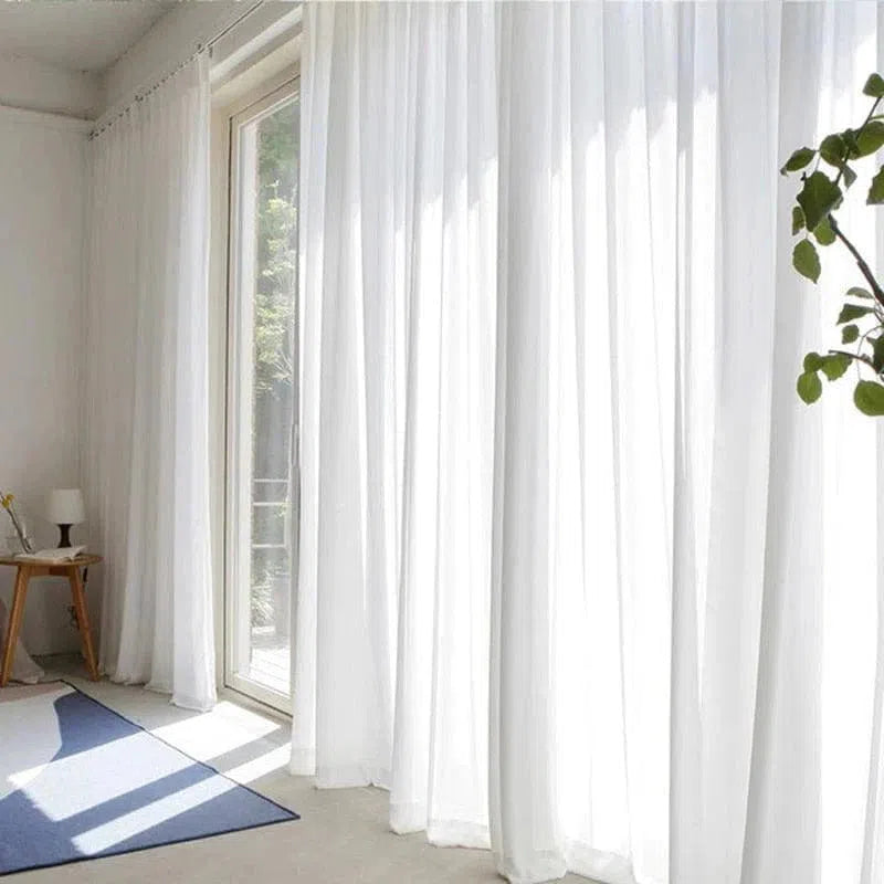 Rideaux blancs élégants dans un salon lumineux, apportant une ambiance douce et moderne. Ces rideaux filtraient la lumière naturelle, offrant une intimité subtile. Un choix idéal pour une décoration intérieure contemporaine, ces rideaux mettent en valeur un espace éclairé et accueillant, avec un mobilier minimaliste en arrière-plan et une plante verte ajoutant une touche de fraîcheur.