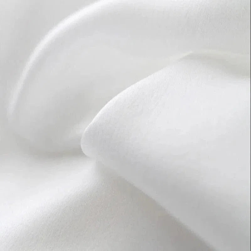 Texture de tissu blanc en gros plan, montrant des plis doux et élégants, idéal pour la literie ou la confection de vêtements confortables.
