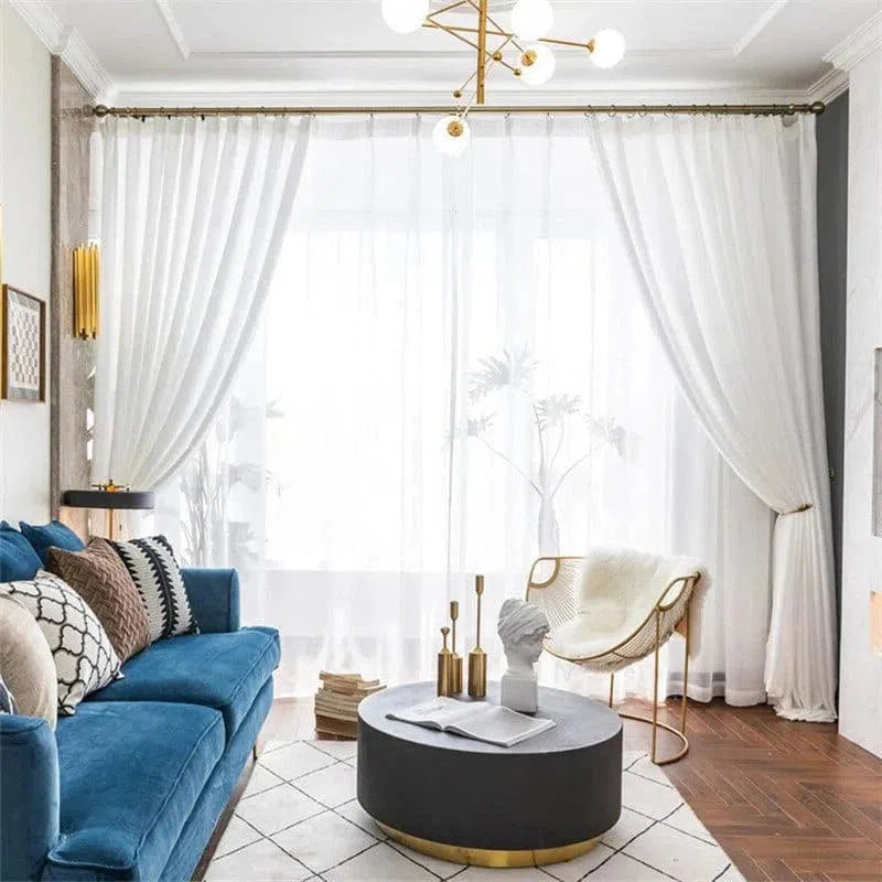 Salon contemporain et élégant avec canapé bleu, table basse ronde noire, chaise moderne et rideaux blancs légers. Décoration intérieure sophistiquée dans un espace lumineux mettant en valeur des détails dorés subtils. Idéal pour une ambiance chic et accueillante.