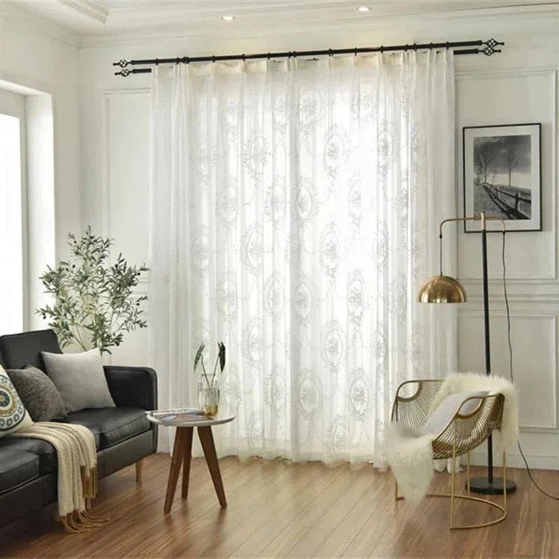 Voilage élégant blanc avec motifs décoratifs dans un salon moderne, agrémenté d'un canapé noir aux coussins colorés et d'une lampe dorée. Ajoutez une touche de sophistication à votre intérieur avec ces rideaux lumineux qui filtrent la lumière tout en préservant l'intimité. Accessoires de décoration inclus pour une ambiance chic et contemporaine.