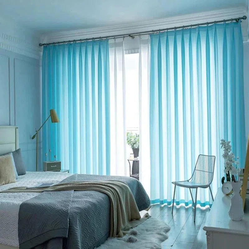 Chambre moderne avec rideaux bleus translucides, offrant une ambiance lumineuse et aérée. Parfait pour créer un espace de repos paisible et élégant. Le lit confortable est agrémenté de couvertures douillettes, et une décoration minimaliste complète le look contemporain de la pièce.  Un coin détente avec une chaise design ajoute une touche de sophistication.