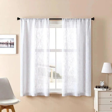 Voilage blanc élégant pour salon, installée sur une tringle noire. Décoration intérieure moderne avec chaise design, lampe de chevet et tableau encadré sur mur beige. Idéal pour filtrer la lumière naturelle tout en préservant l'intimité de votre espace de vie.
