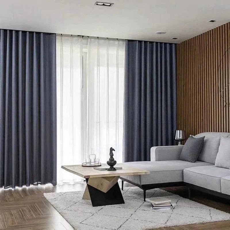 Rideaux élégants dans un salon moderne et épuré, parfaits pour créer une ambiance chaleureuse et raffinée. Idéal pour ceux qui cherchent à embellir leur intérieur avec style. Meuble d'angle gris confortable, posé sur un tapis clair, apporte une touche de confort à l'espace de vie.
