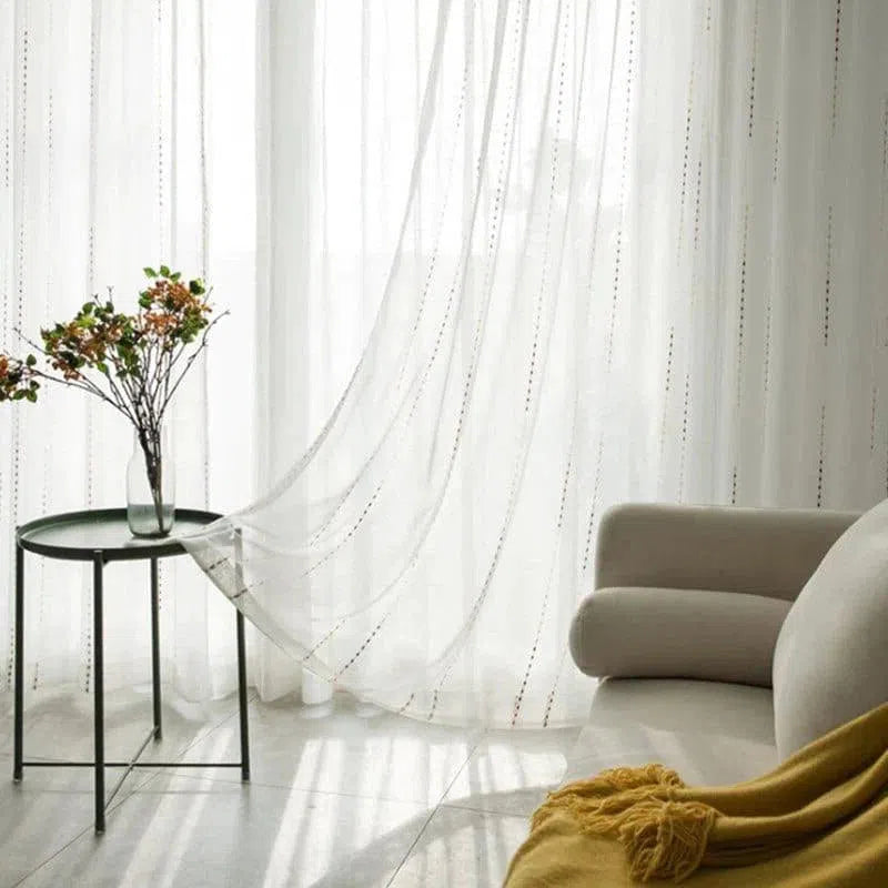 Voilage élégant et raffiné laissant passer la lumière naturelle dans un salon moderne, table d'appoint avec vase fleuri et canapé accueillant, créant une ambiance chaleureuse et apaisante. Parfait pour ajouter une touche de douceur à votre décoration intérieure.