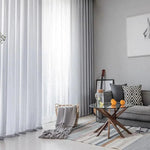 Salon moderne et lumineux avec rideaux élégants, mobilier design, et accents décoratifs contemporains. Atmosphère accueillante avec tapis rayé, table basse en verre, coussins géométriques, et une guitare en arrière-plan. Décoration intérieure chic et confortable.