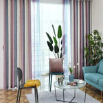 Rideaux multicolores élégants ornant un salon moderne, avec une décoration intérieure harmonieuse comprenant un canapé bleu, un fauteuil assorti, et une table basse contemporaine agrémentée d'objets décoratifs. La pièce est illuminée par une lumière naturelle venant de grandes fenêtres avec des rideaux semi-transparents, créant une ambiance chaleureuse et accueillante.