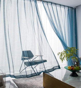 Rideaux élégants bleus dans un salon moderne avec fauteuil assorti. Lumière naturelle filtrée créant une ambiance apaisante. Décoration design avec table basse et plante verte. Parfait pour ajouter une touche contemporaine à votre intérieur.