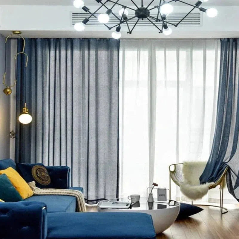 Salon moderne avec un canapé bleu stylé, accentué par des coussins jaunes et une lumière douce. Les rideaux bleus apportent une touche élégante, harmonisée avec des éléments de décoration chic comme le lustre contemporain. Un espace accueillant et tendance pour une ambiance confortable.
